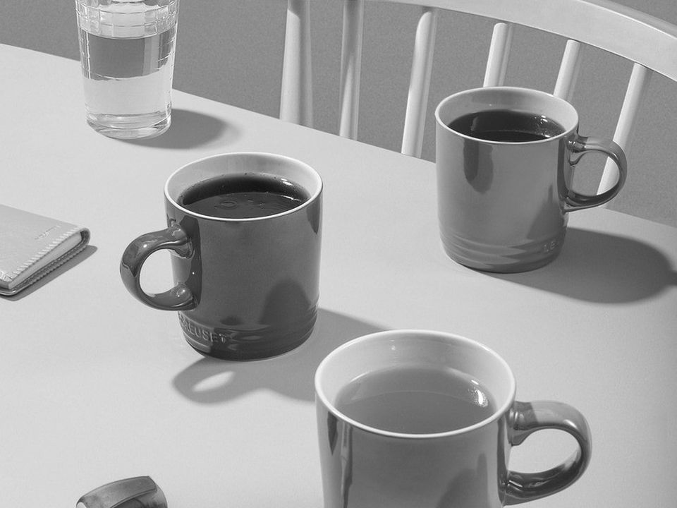 Two white coffee cups on a wooden table in early morning light