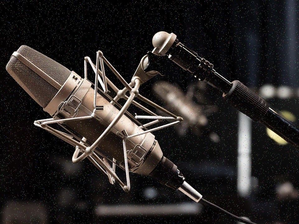 A studio microphone with a foam windscreen on a boom arm in front of a dark acoustic panel