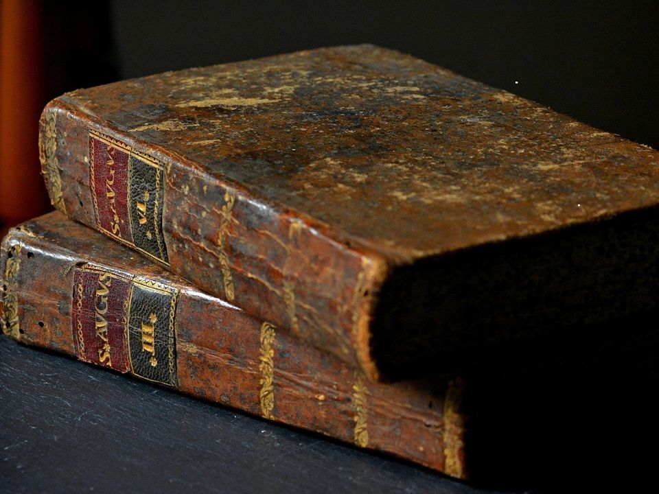 A stack of worn clothbound books with faded spines resting on a wooden table